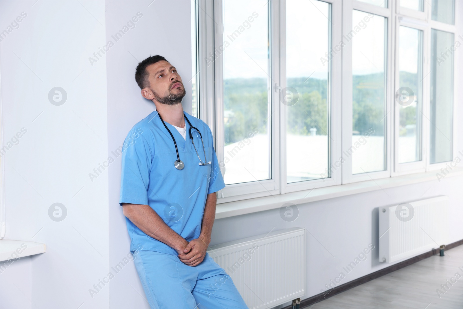 Photo of Exhausted doctor near white wall in hospital hallway