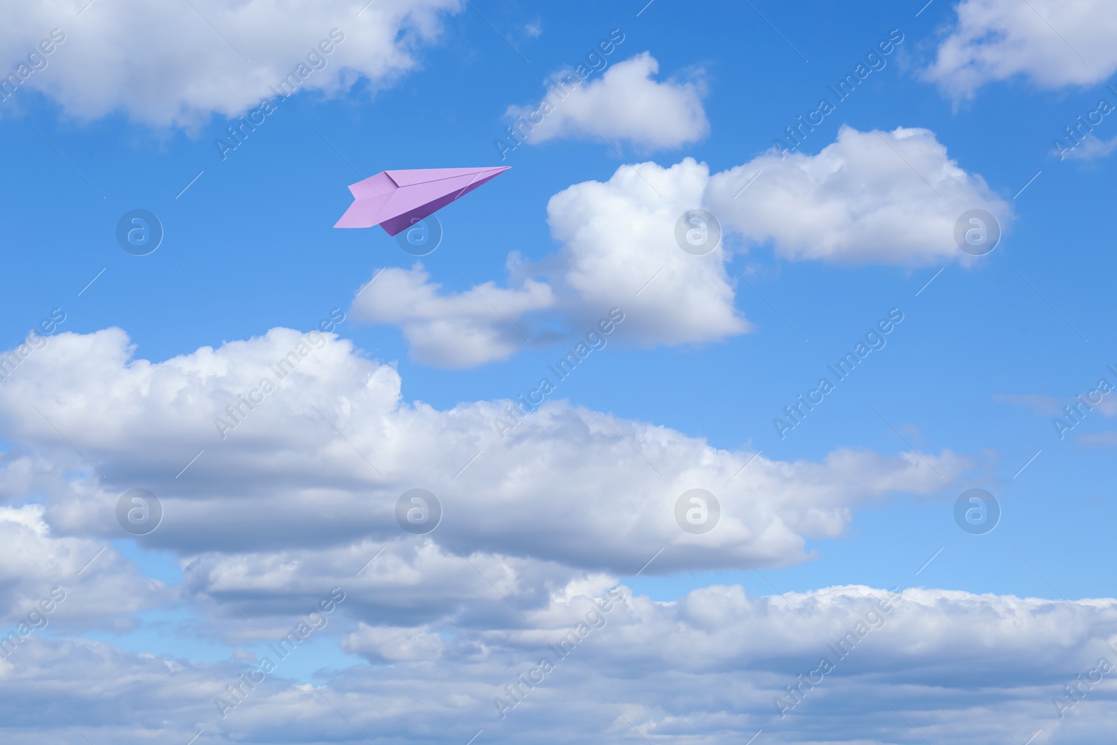 Image of Violet paper plane flying in blue sky with clouds