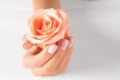 Closeup view of woman with rose at white table, space for text. Spa treatment