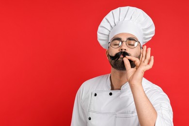 Photo of Professional chef with funny artificial moustache showing perfect sign on red background. Space for text
