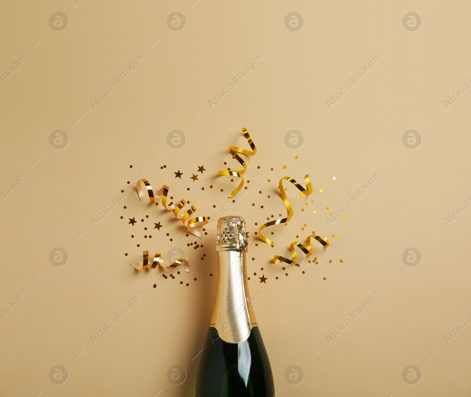 Photo of Bottle of champagne with gold glitter and confetti on beige background, flat lay. Hilarious celebration
