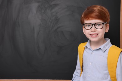 Smiling schoolboy in glasses near blackboard. Space for text
