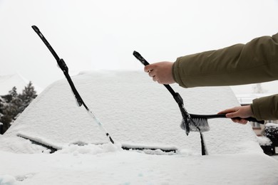 Photo of Woman cleaning car wiper blade from snow with brush outdoors, closeup