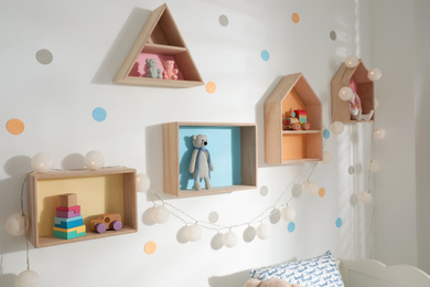 Photo of Colorful house shaped shelves on white wall indoors. Children's room interior design