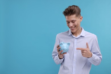 Photo of Happy man pointing at piggy bank on light blue background. Space for text