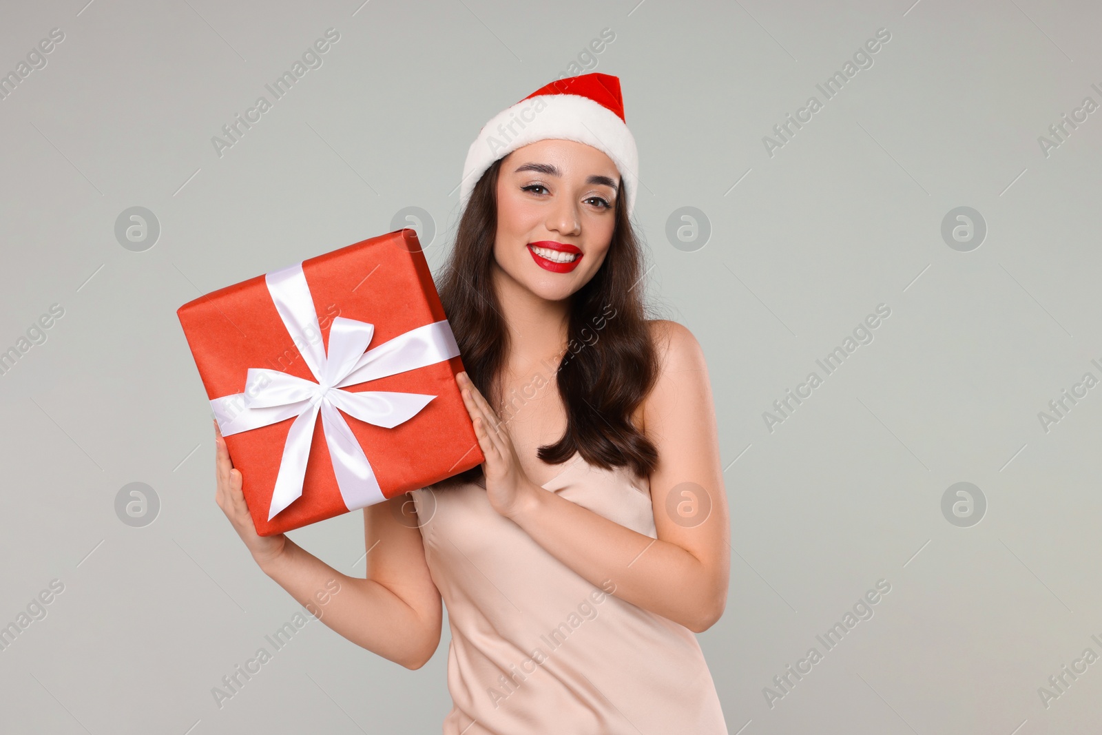 Photo of Beautiful young woman in Santa hat with Christmas gift on grey background