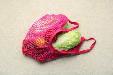 Photo of Fresh Chinese cabbage and other products in string bag on light textured table