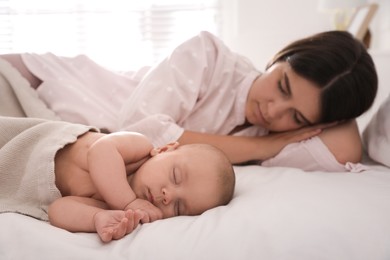 Photo of Young mother resting near her sleeping baby on bed at home