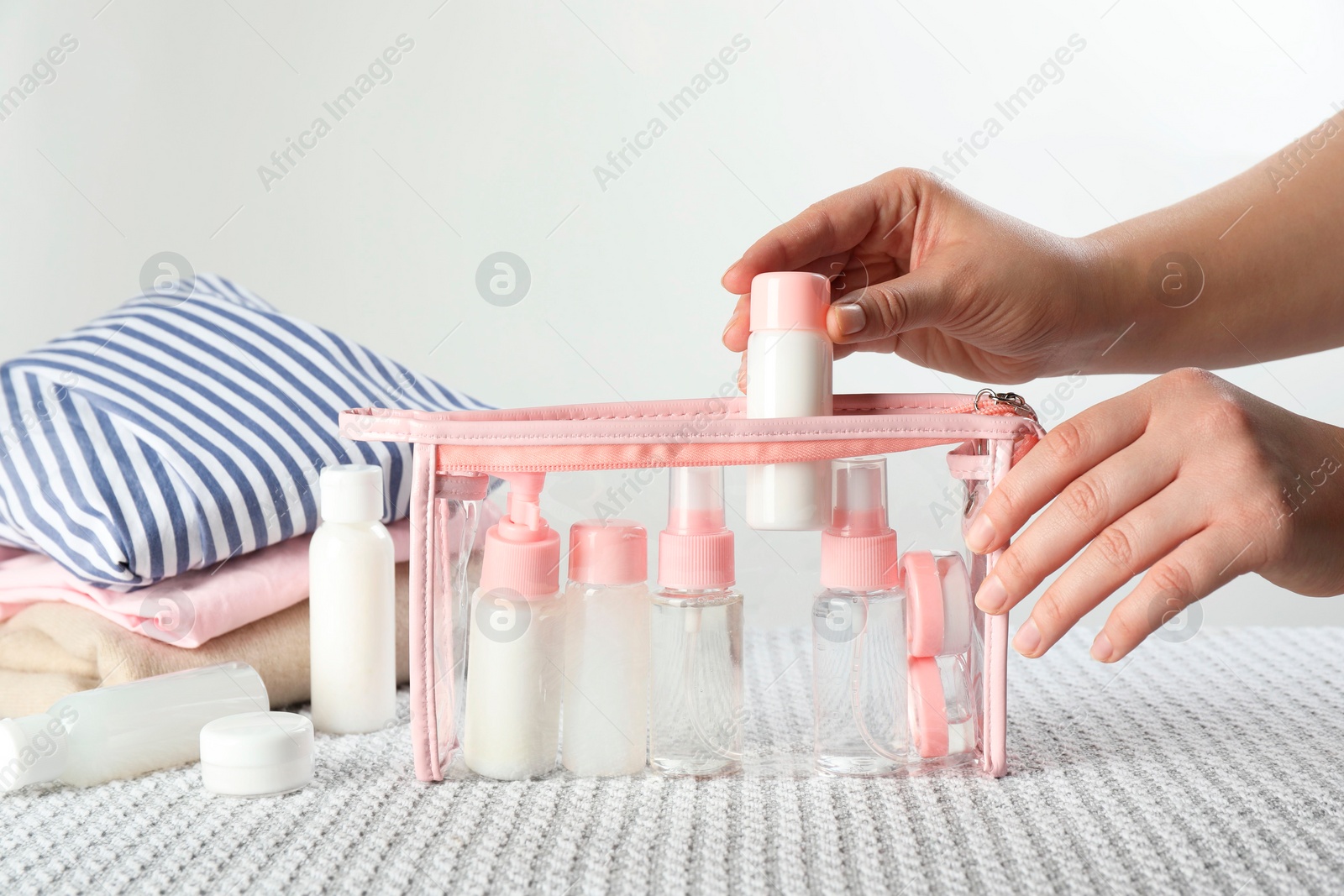 Photo of Woman putting small bottle with personal care product into plastic bag, closeup. Cosmetic travel kit