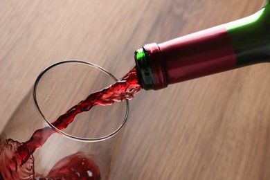 Pouring tasty red wine in glass at wooden table, closeup