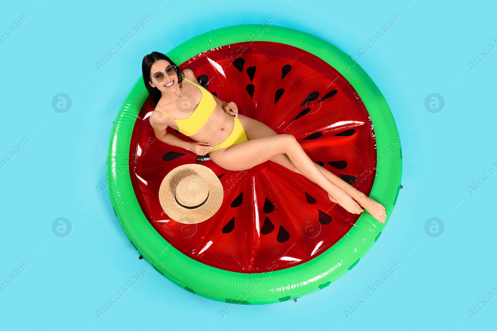 Photo of Young woman with stylish sunglasses on inflatable mattress against light blue background, above view