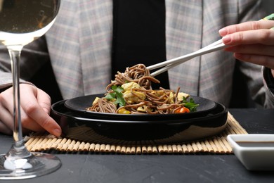 Photo of Stir-fry. Woman eating tasty noodles with meat and vegetables at dark textured table, closeup