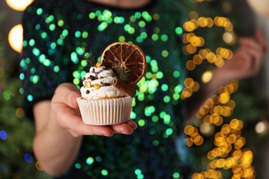 Woman with Christmas cupcake against blurred festive lights, closeup