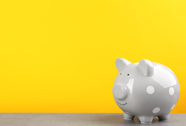 Photo of Grey piggy bank on light grey table against yellow background. Space for text