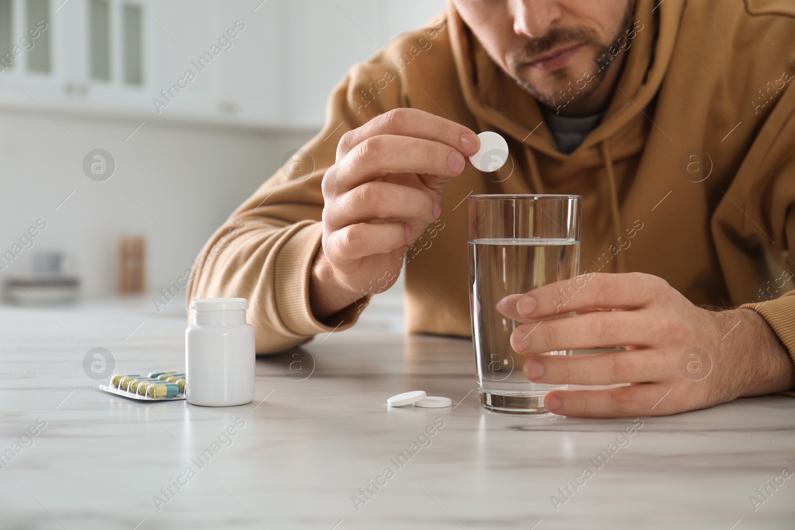 Photo of Man taking medicine for hangover at table in kitchen, closeup