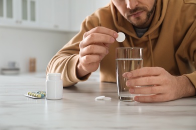 Photo of Man taking medicine for hangover at table in kitchen, closeup