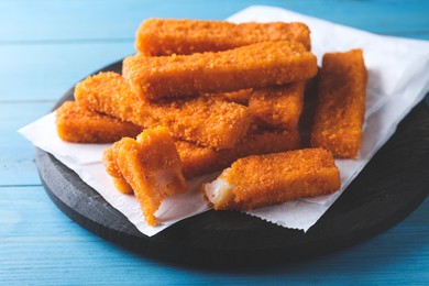 Photo of Fresh breaded fish fingers served on light blue wooden table