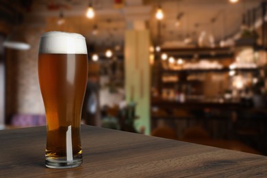 Image of Glass with fresh beer on wooden table in pub, space for text