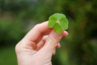 Photo of Woman holding beautiful green four leaf clover outdoors, closeup