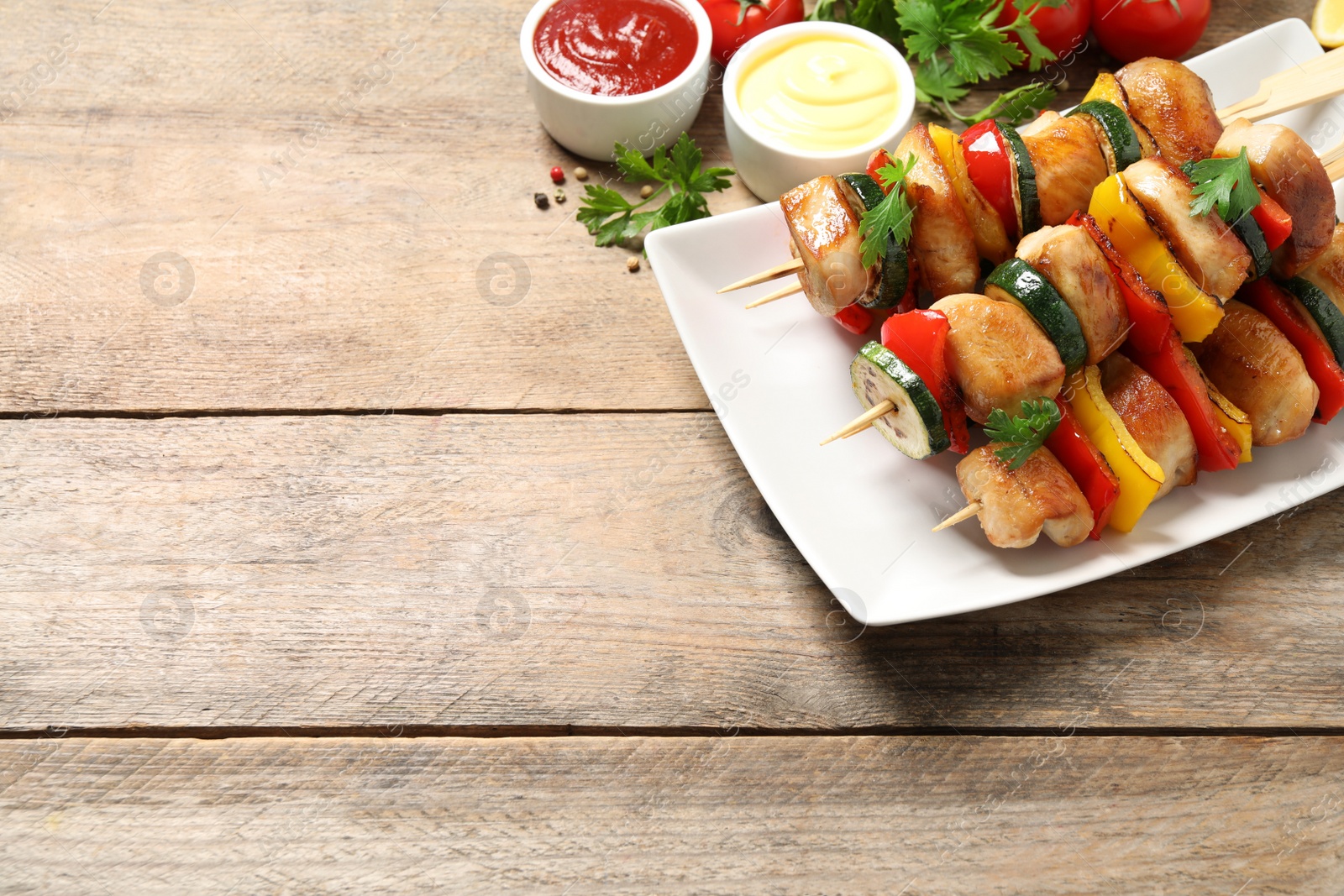 Photo of Delicious chicken shish kebabs with vegetables and sauce on wooden table. Space for text