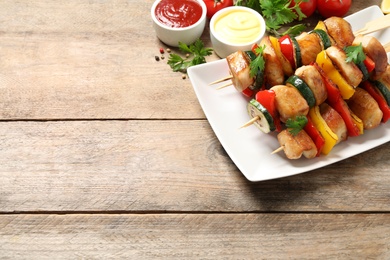 Delicious chicken shish kebabs with vegetables and sauce on wooden table. Space for text