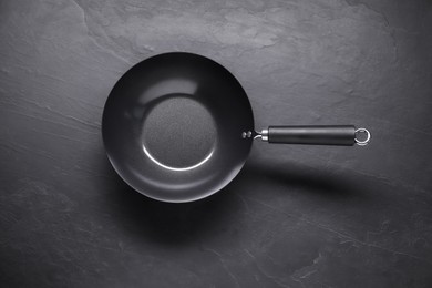 Photo of Empty iron wok on black textured table, top view. Chinese cookware