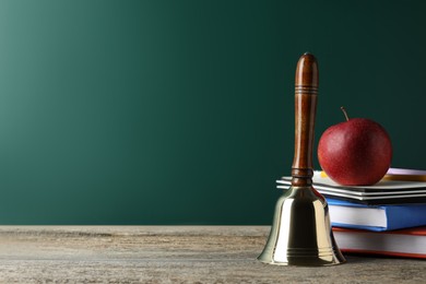 Golden school bell, apple and books on wooden table near green chalkboard. Space for text