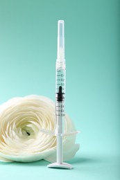 Photo of Cosmetology. Medical syringe and ranunculus flower on turquoise background