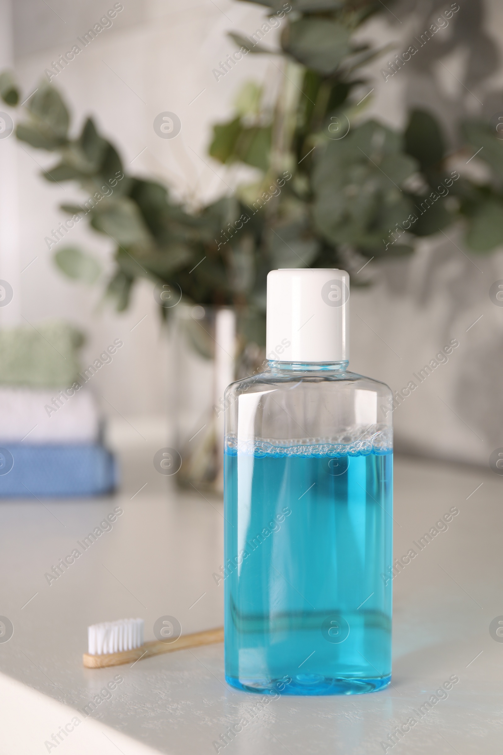 Photo of Bottle of mouthwash and toothbrush on white table in bathroom