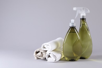 Bottles of cleaning product and rolled rags on light background. Space for text