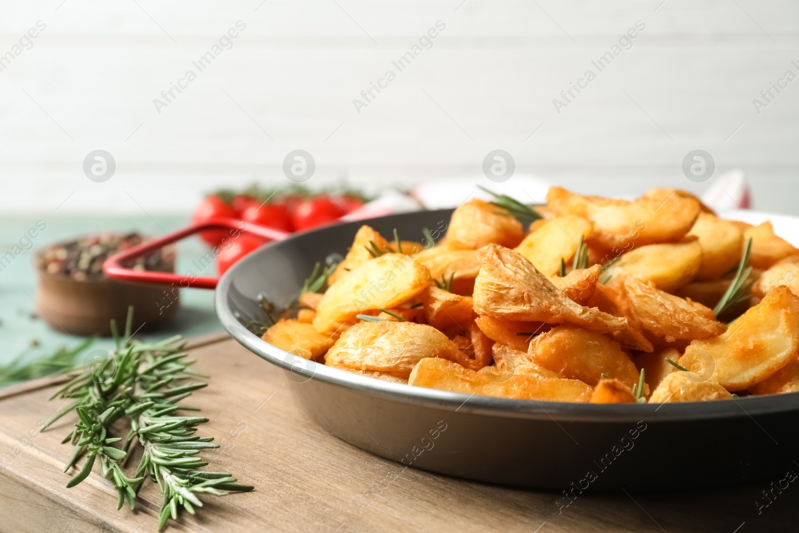 Photo of Dish with baked potatoes and rosemary in wok on wooden board, closeup