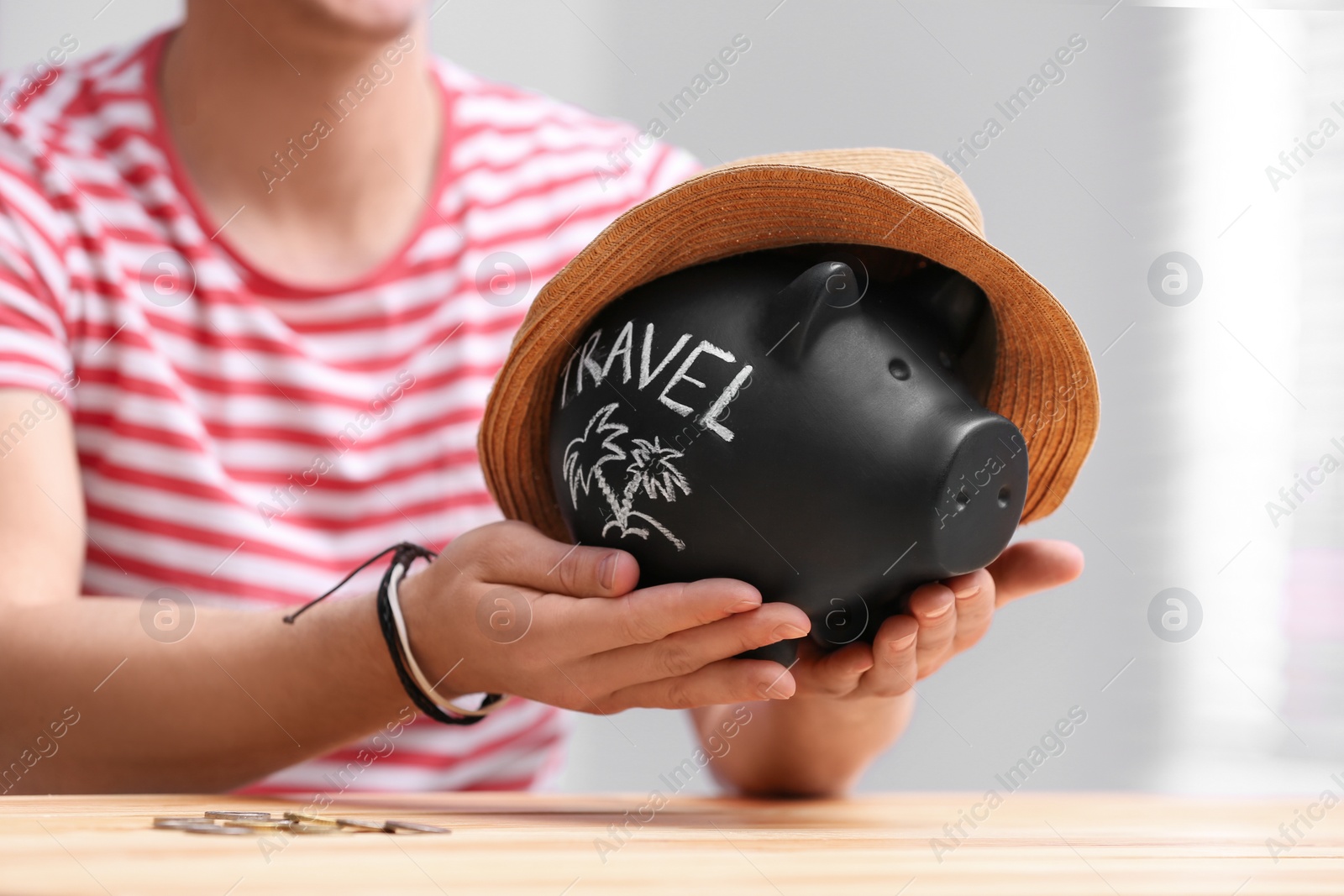 Photo of Man holding piggy bank with word TRAVEL and hat at table, closeup