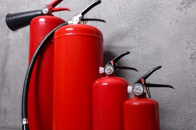 Four red fire extinguishers near grey wall