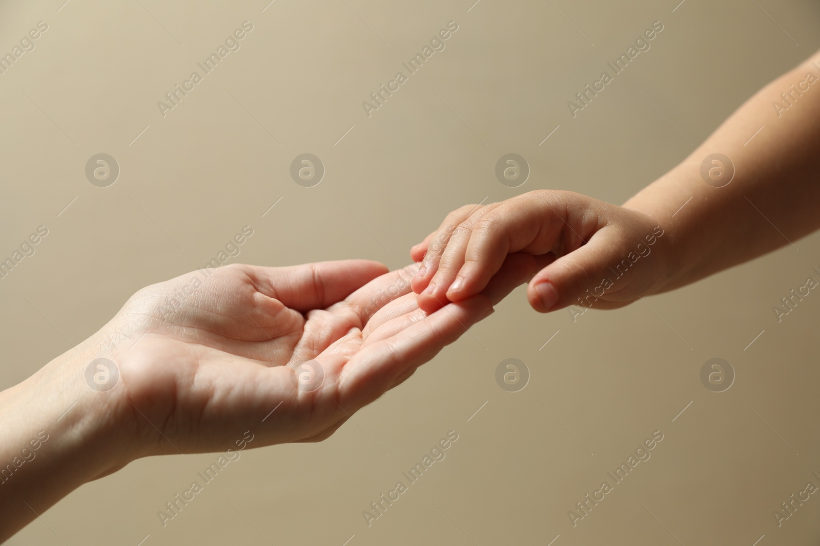 Photo of Mother and child holding hands on beige background, closeup