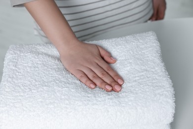 Woman touching soft white towel indoors, closeup