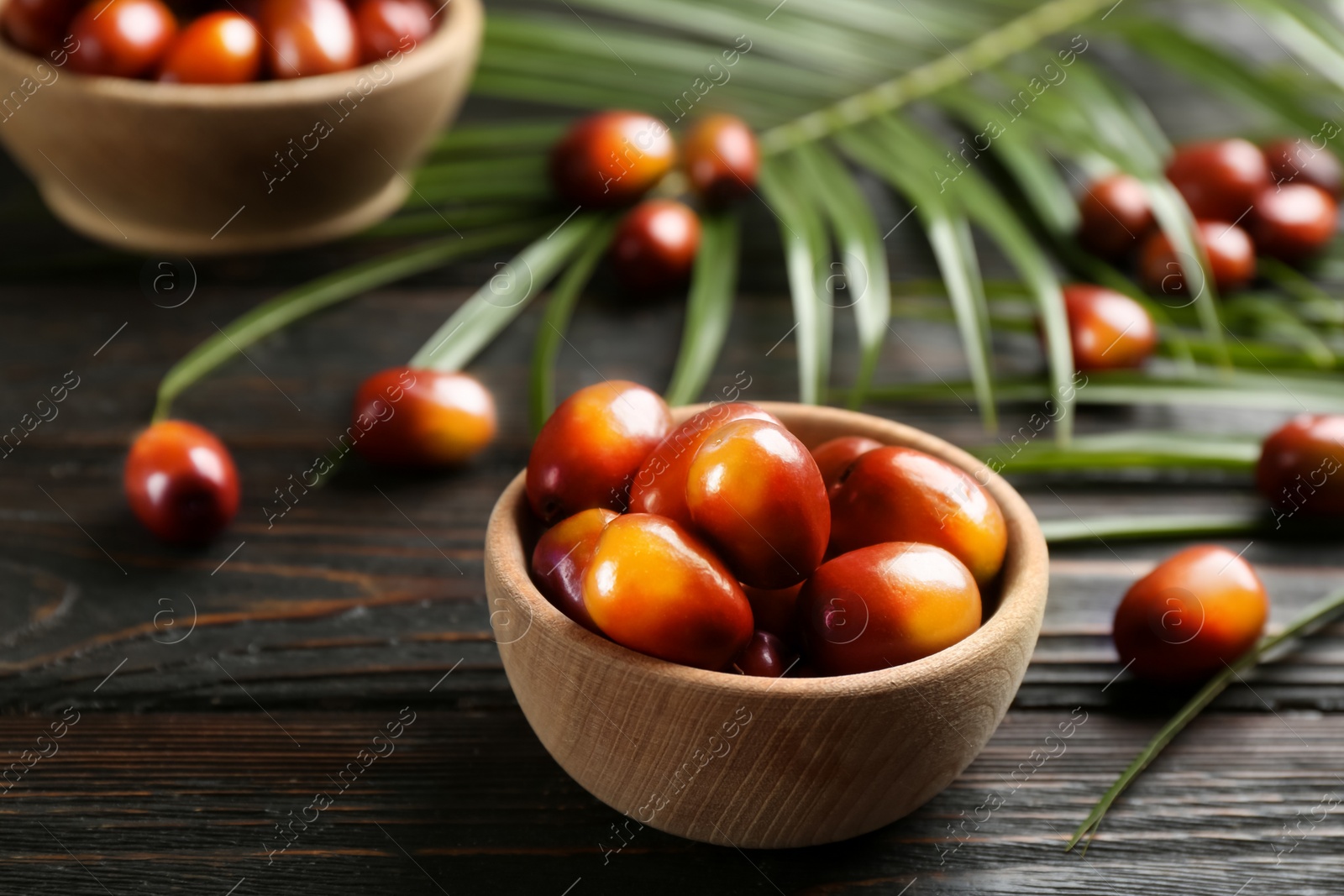 Image of Palm oil fruits in bowl on black wooden table, closeup