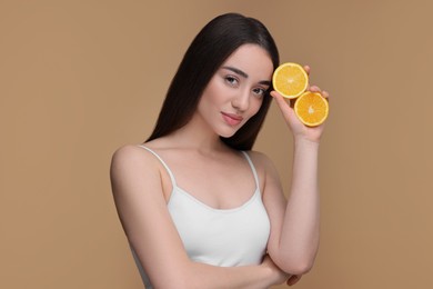 Beautiful young woman with pieces of orange on beige background