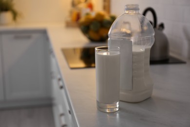 Gallon bottle of milk and glass on white countertop in kitchen. Space for text