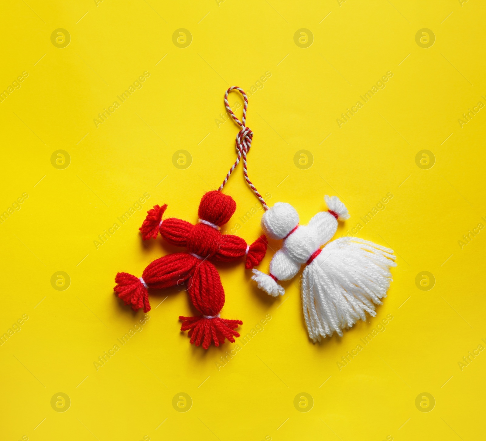 Photo of Traditional martisor shaped as man and woman on yellow background, top view. Beginning of spring celebration