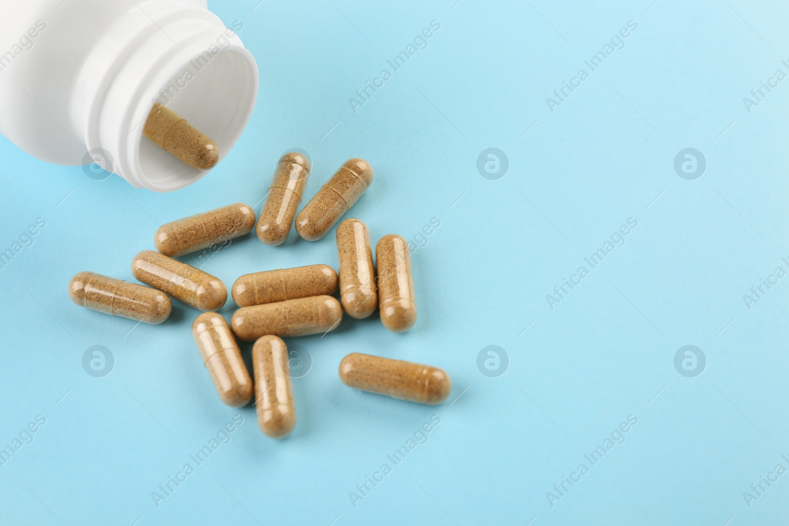 Photo of Bottle and vitamin capsules on light blue background, closeup. Space for text