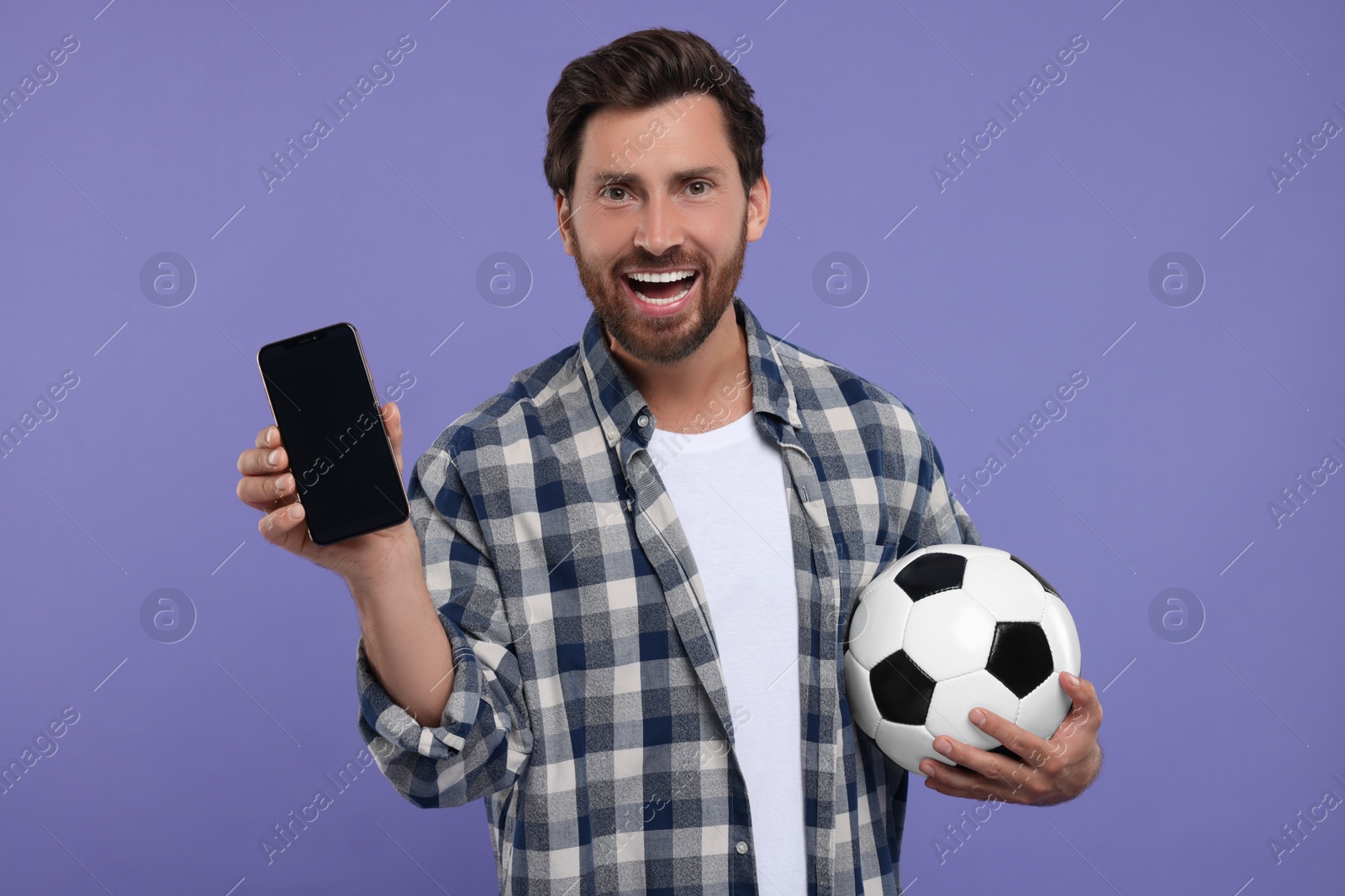 Photo of Happy sports fan with soccer ball and smartphone on purple background