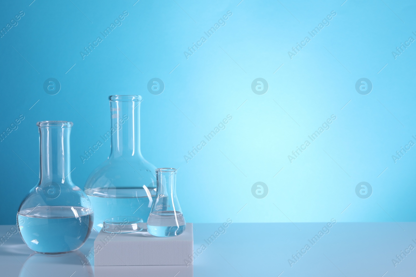 Photo of Laboratory analysis. Glass flasks on table against light blue background, space for text