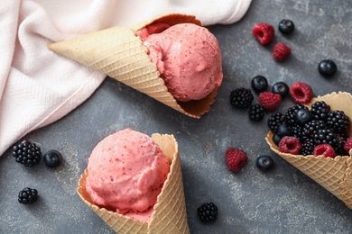 Flat lay composition with delicious pink ice cream in wafer cones and berries on grey table