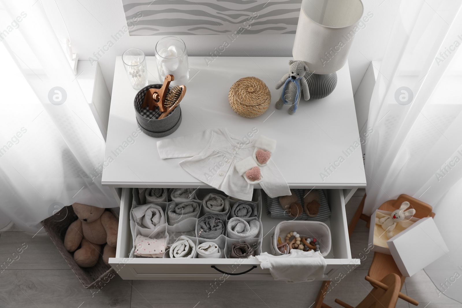 Photo of Modern open chest of drawers with baby clothes and accessories in room, above view