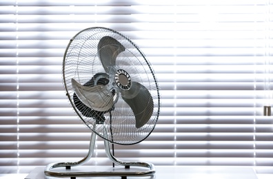 Photo of Modern electric fan on table near window indoors. Space for text
