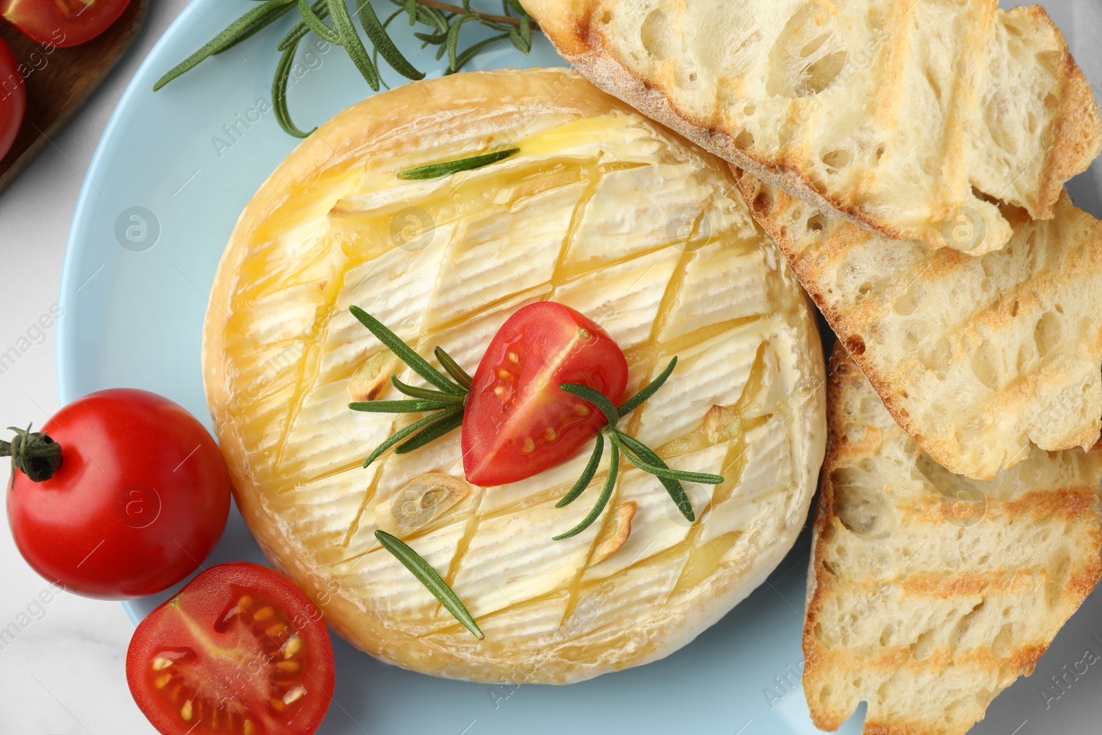 Photo of Tasty baked brie cheese with rosemary, cherry tomatoes and bread on plate, top view