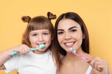 Photo of Little girl and her mother brushing teeth together on color background