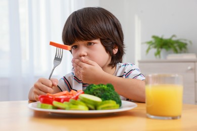 Photo of Cute little boy covering mouth and refusing to eat vegetables at home