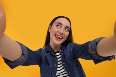 Photo of Young woman taking selfie and showing tongue on yellow background