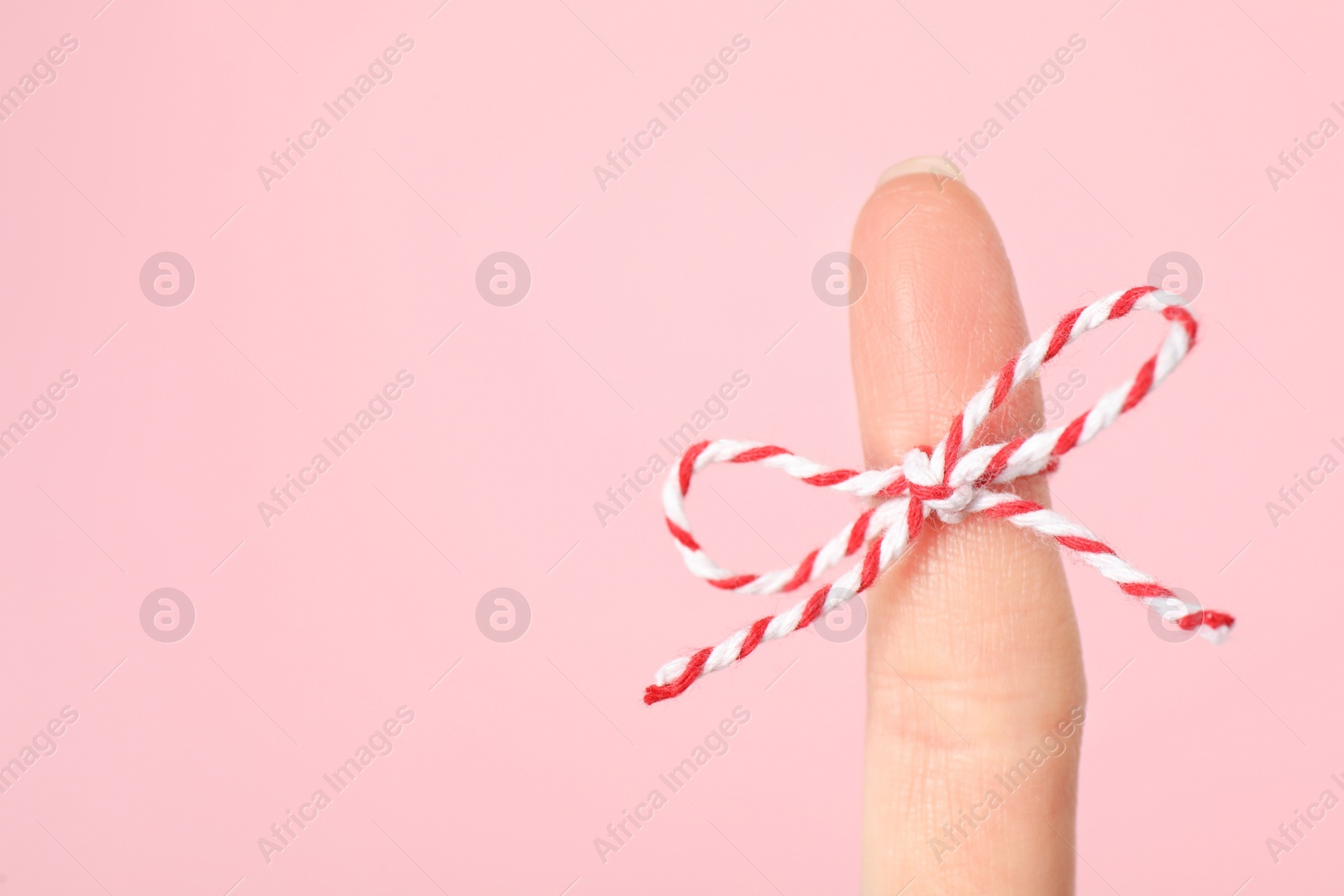 Photo of Woman showing index finger with tied bow as reminder on pink background, closeup. Space for text